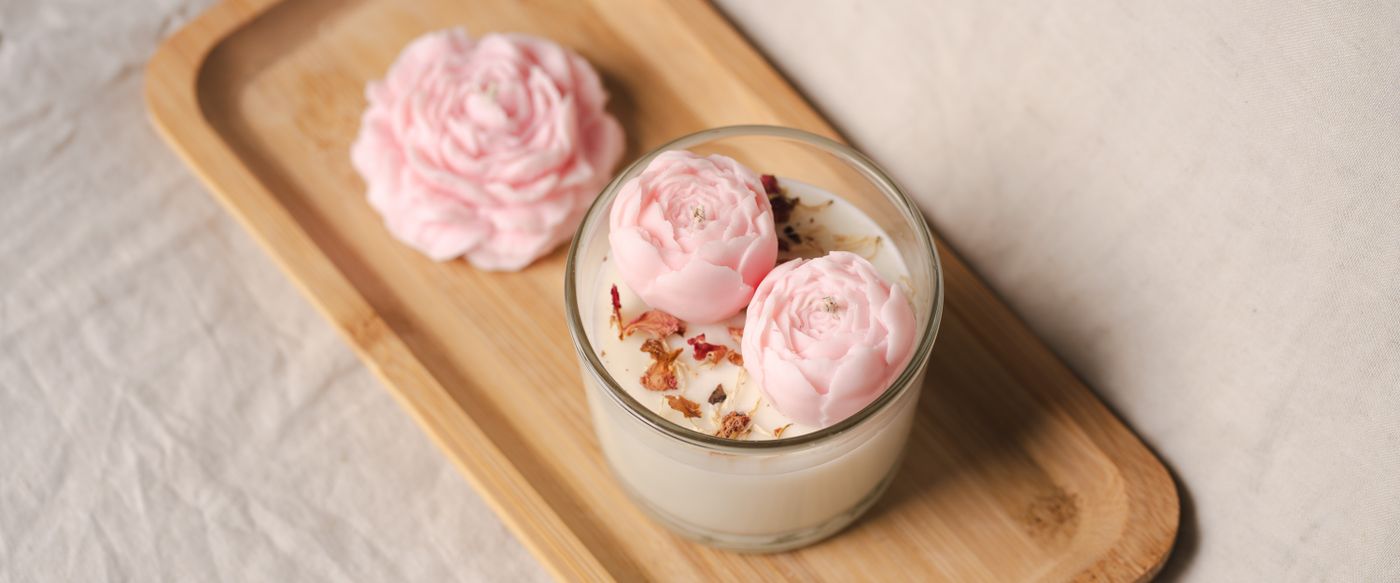 A floral candle glowing among pink flowers, an example of strong scented candles at home