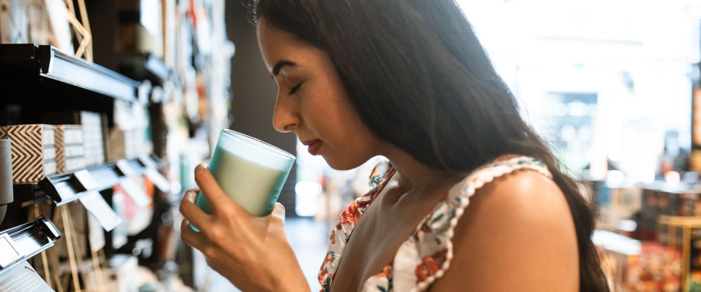 Woman smelling a scented candle jar, checking candle fragrance in a bright shop