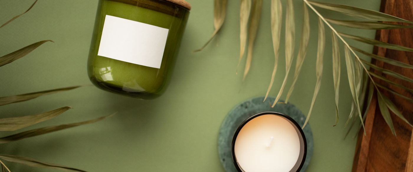 Green jar candle and a lit candle among leaves, for best rated scented candles