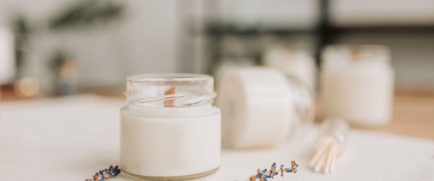 A lit lavender candle beside dried flowers on a soft spring table