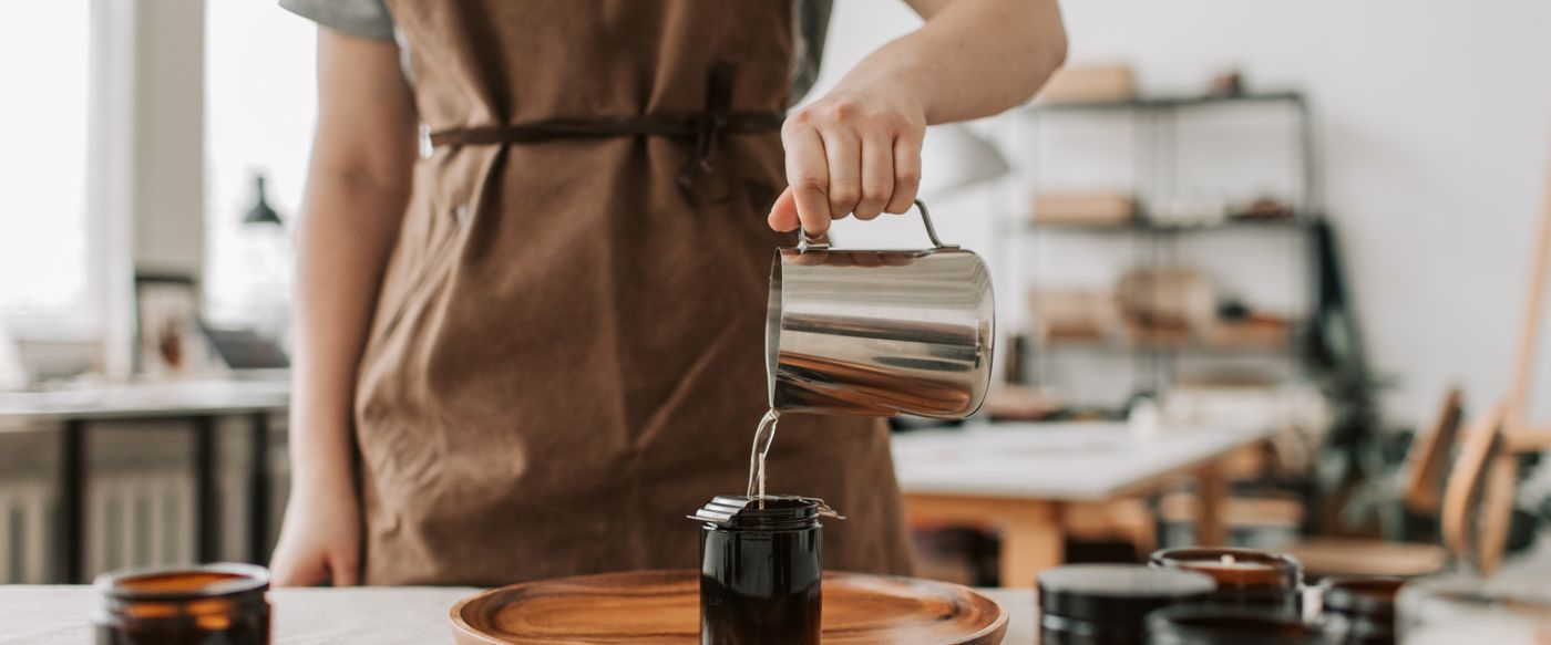 A maker pours wax into jars, the first step in triple scented candles