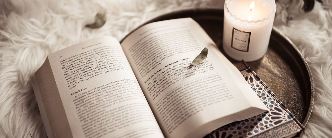 Candles and fragrances set beside an open book for a cosy evening read