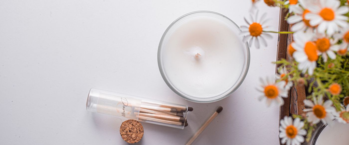 Lit candle with fresh daisies and matches, showing the natural side of candle scent oil