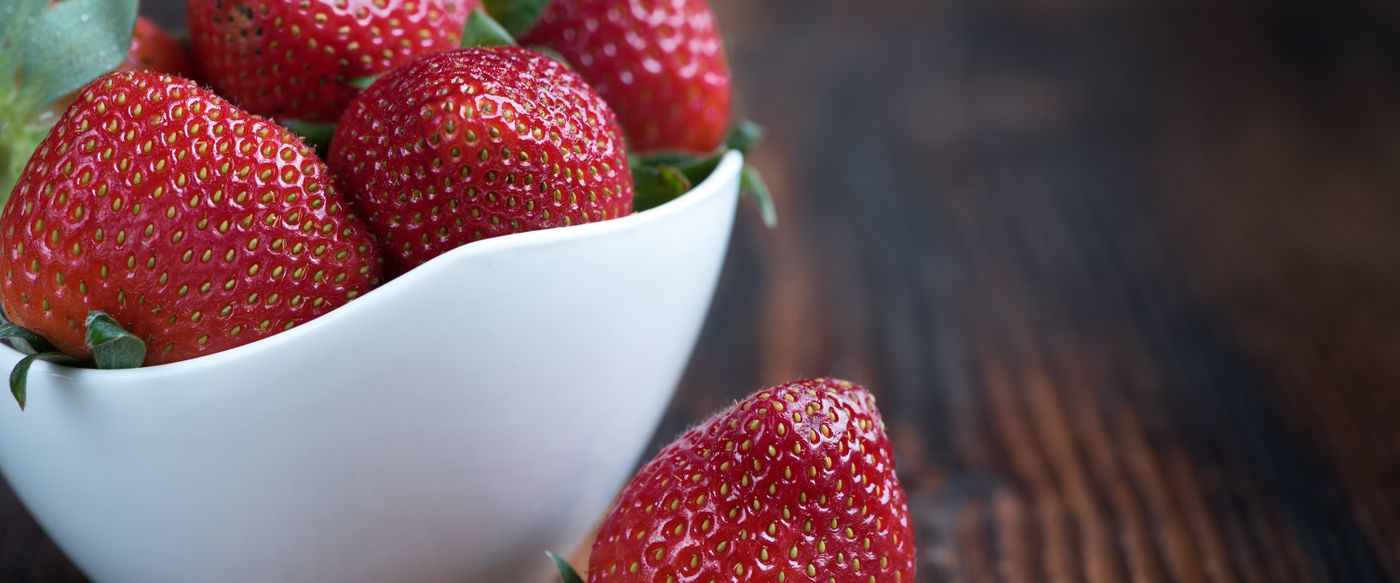 Fresh strawberries in a white bowl on a wooden table, the fruit behind fruity candles